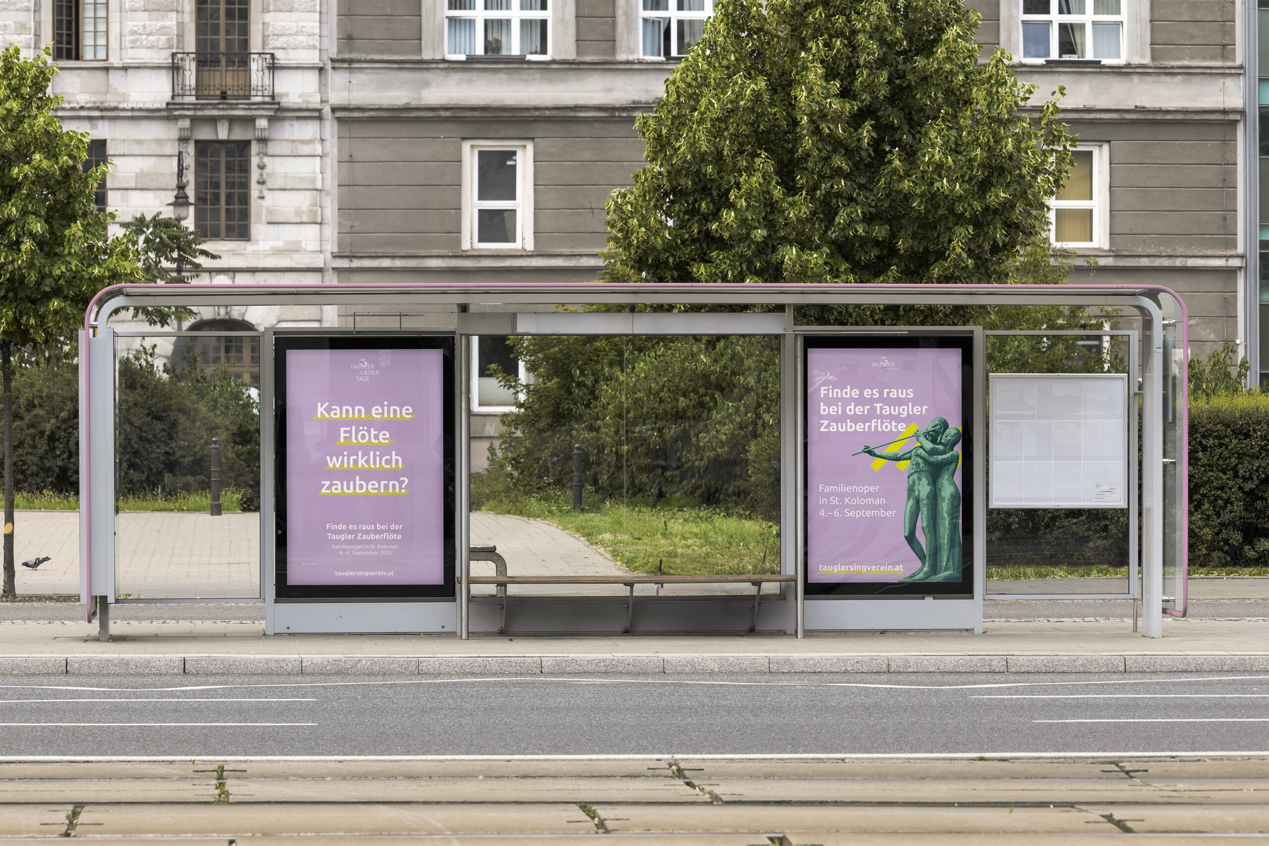 Eine Straßenbahnhaltestelle mit zwei violetten Plakaten auf Deutsch, dahinter Bäume und eine leere Bank im Wartehäuschen. Im Vordergrund sind die Straße und die Straßenbahnschienen zu sehen.